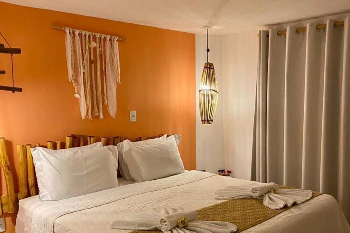 A hotel room with a bed, a ceiling fan, a hanging light fixture, and a window with curtains.