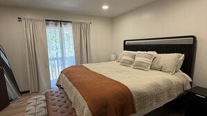 Um quarto com cama, um banco, uma mesa de cabeceira, uma janela com cortinas e uma escada.