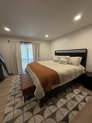 A bedroom with a bed, a bench, a nightstand, a window with curtains, and a staircase. - Modern retreat near Lake Michigan and Coast Guard Park (Spring Lake)