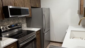 Cozinha equipada com fogão, forno, micro-ondas, frigorífico e armários de madeira.