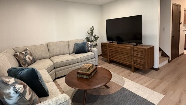Uma sala de estar moderna com um sofá seccional, uma mesa de centro, uma televisão e um armário de madeira.