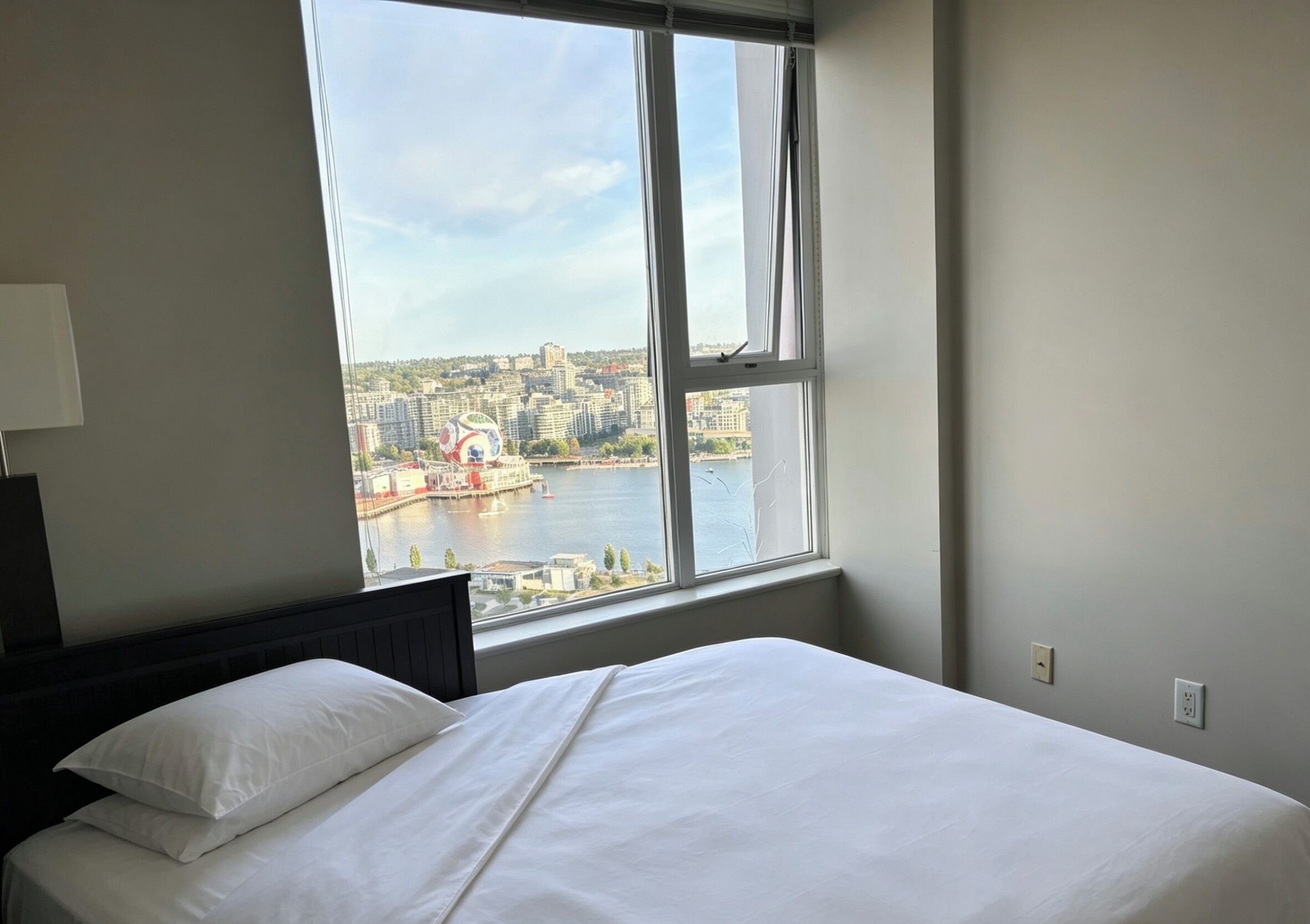 Ein Hotelzimmer mit Bett, Fenster mit Stadtblick und Wandlampe.