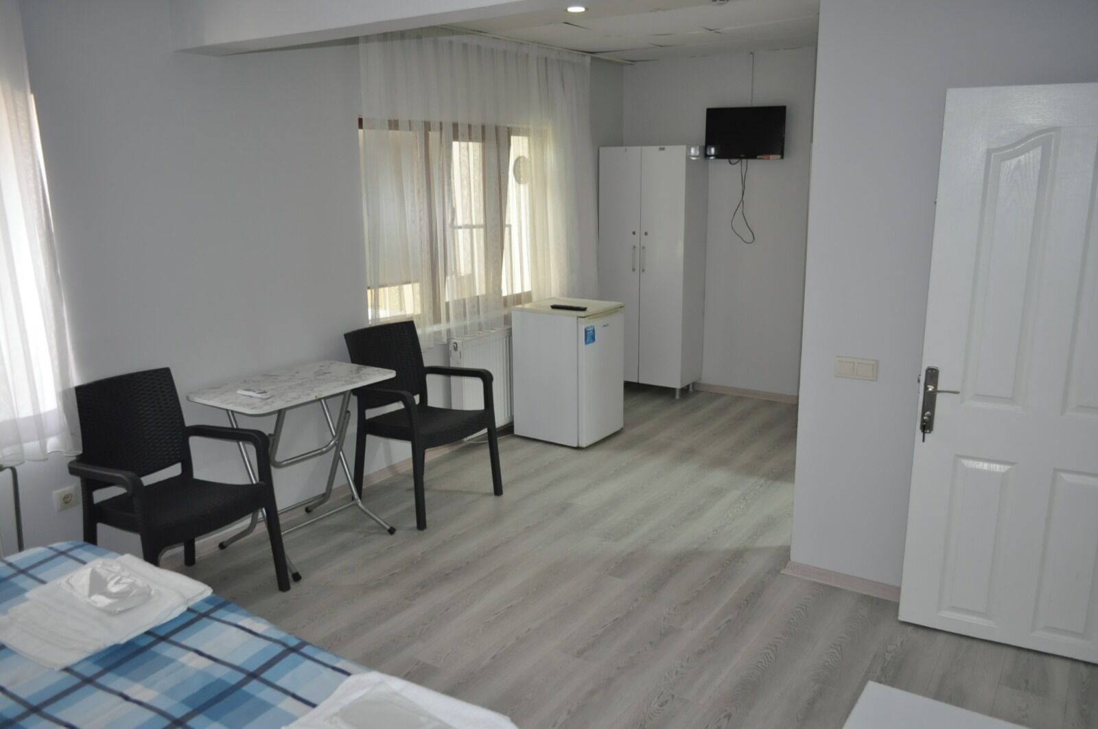 Habitación de hotel con cama, una pequeña mesa con sillas, kitchenette y un televisor montado en la pared, además de una puerta.
