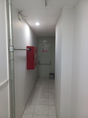 A narrow hallway with a red fire safety box, a metal pipe, a tiled floor, and a door with a no smoking sign. - Bulut Gaye Pansiyon  (Edirne)