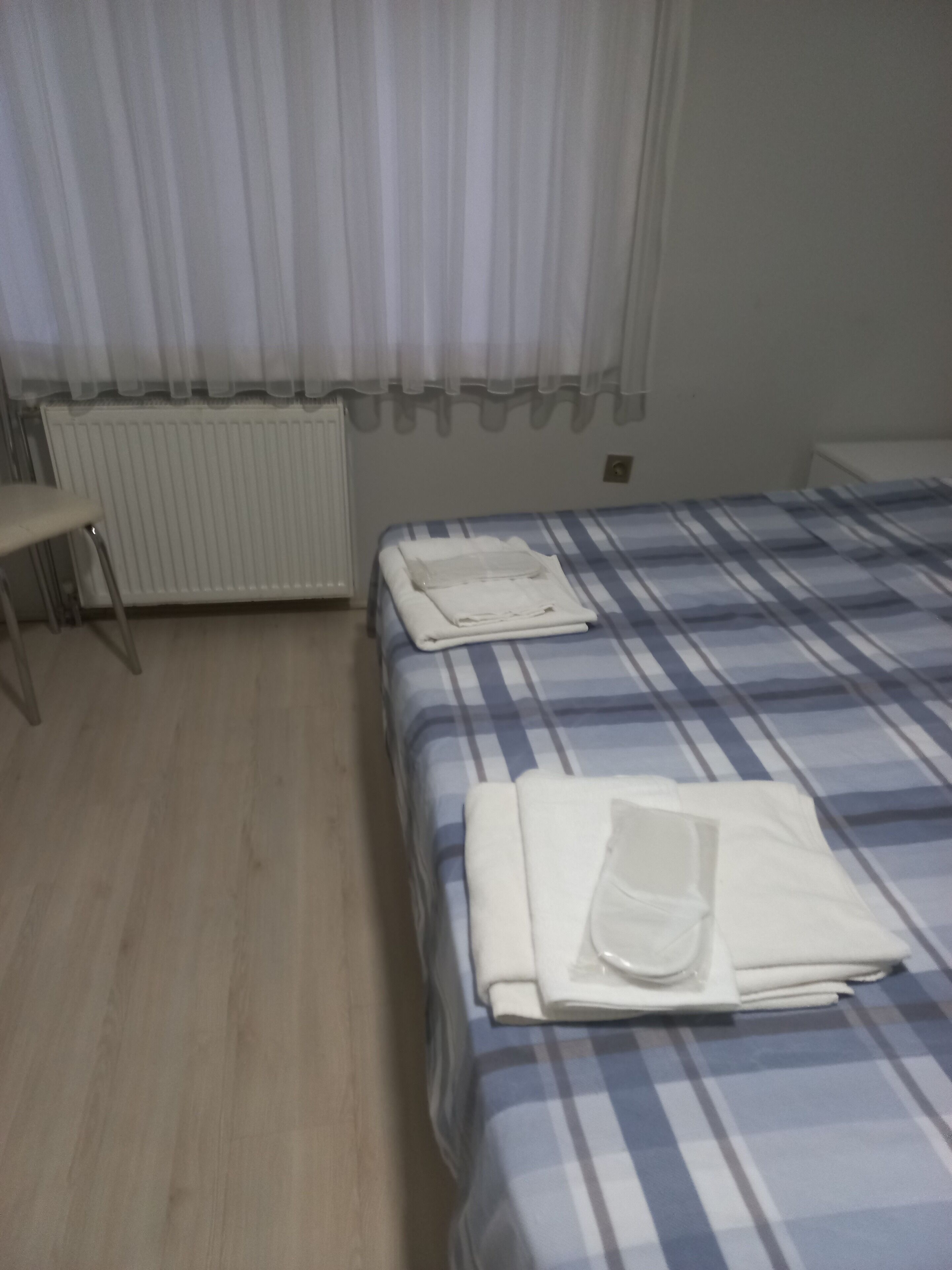 Una habitación con cama, una silla, un radiador y un ventanal con cortinas.