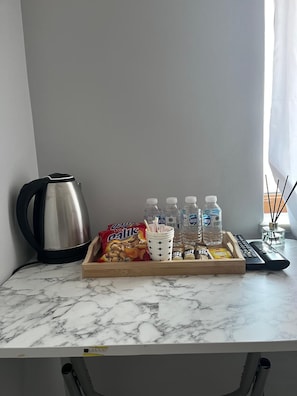 Una encimera de mármol con una bandeja que contiene aperitivos, botellas de agua, una cafetera y un control remoto.