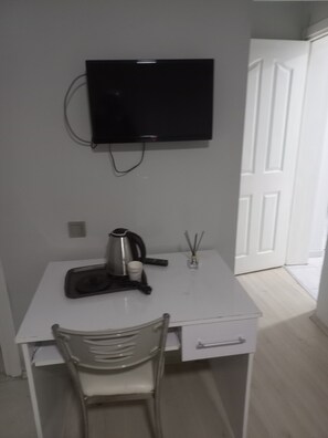 Un escritorio pequeño y blanco con un televisor montado encima, una silla, una cafetera y un adorno pequeño sobre el escritorio.