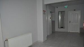 A hallway with a radiator, a door, and an emergency exit sign. - Bulut Gaye Pansiyon  (Edirne)