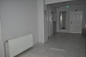 Un couloir avec un radiateur, une porte et un panneau indiquant la sortie de secours.