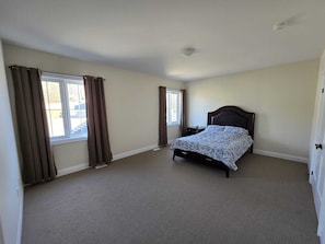 Une chambre à coucher avec un lit, deux fenêtres, un luminaire au plafond et une porte.