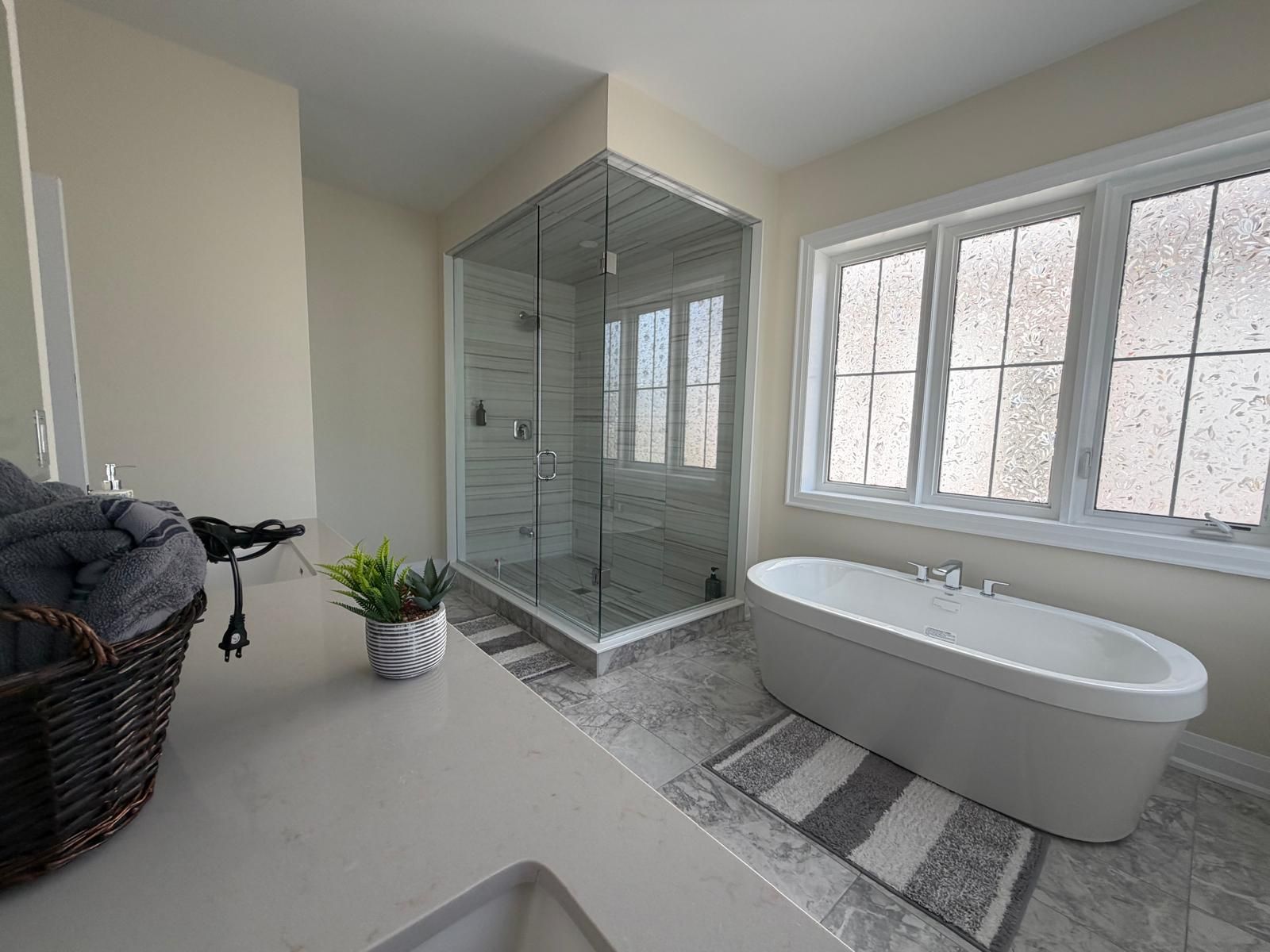 Une salle de bain moderne dotée d’une douche à parois de verre, d’une baignoire sur pieds et d’une grande fenêtre laissant entrer la lumière naturelle.