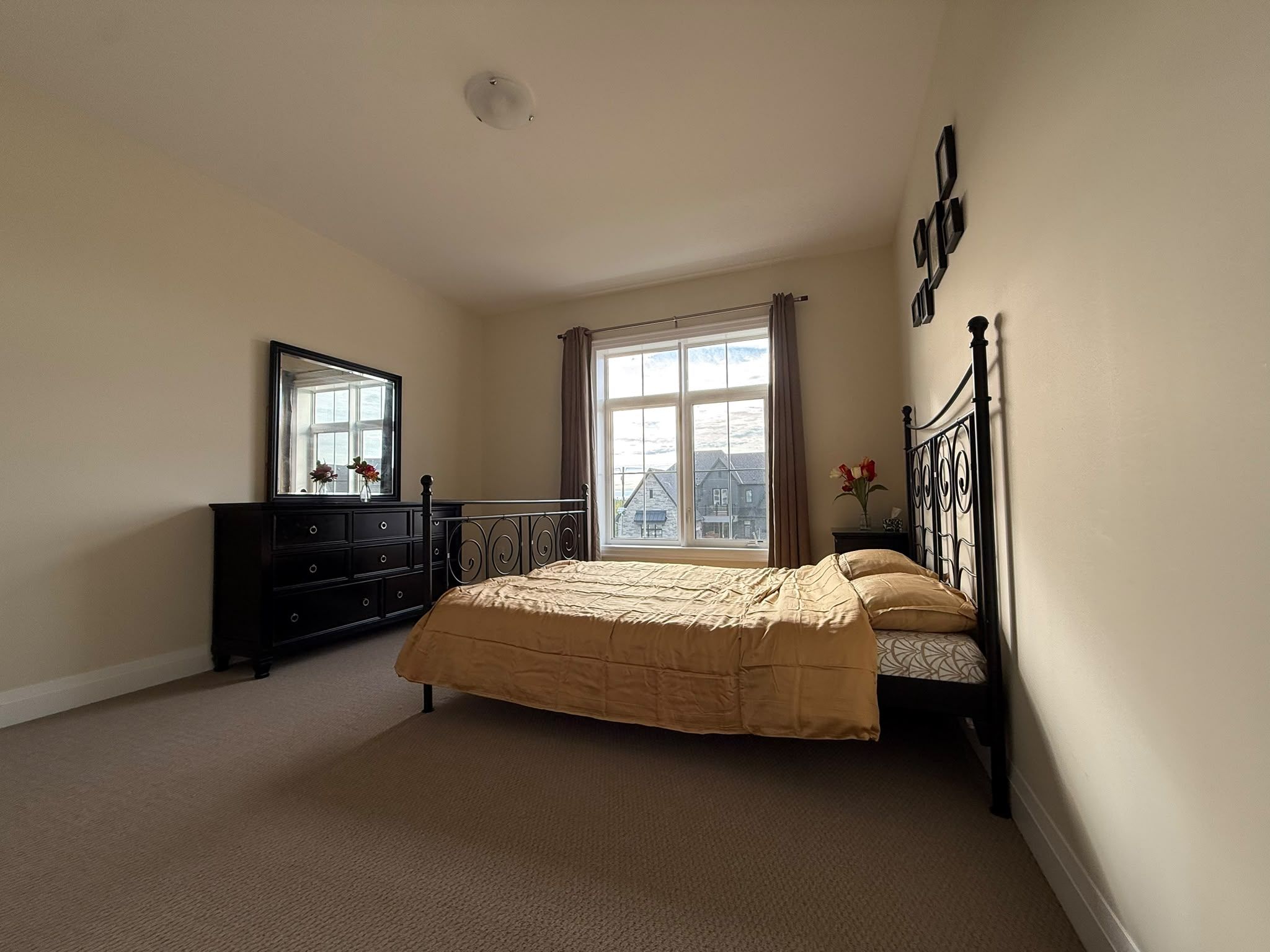 A bedroom with a bed, dresser, mirror, and a window with curtains.