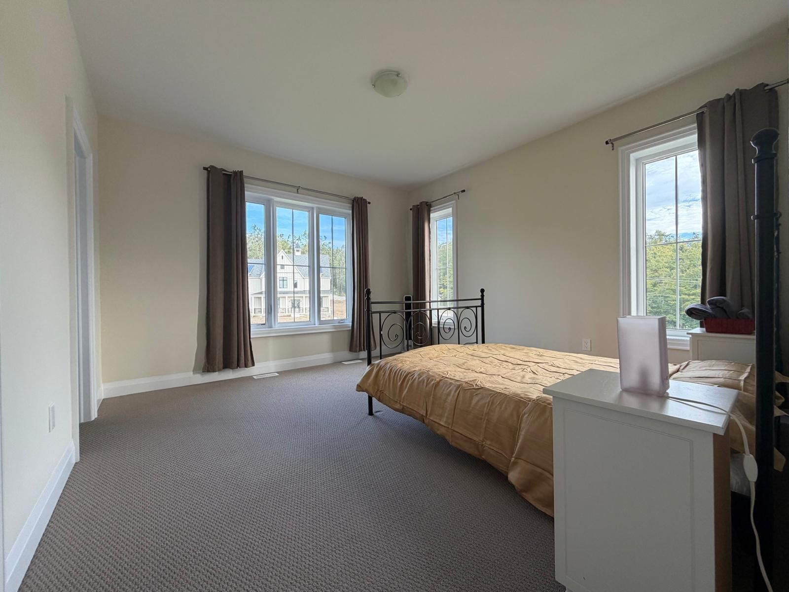 Ein Schlafzimmer mit Bett, Schreibtisch, zwei Fenstern mit Vorhängen und Blick auf ein Haus.