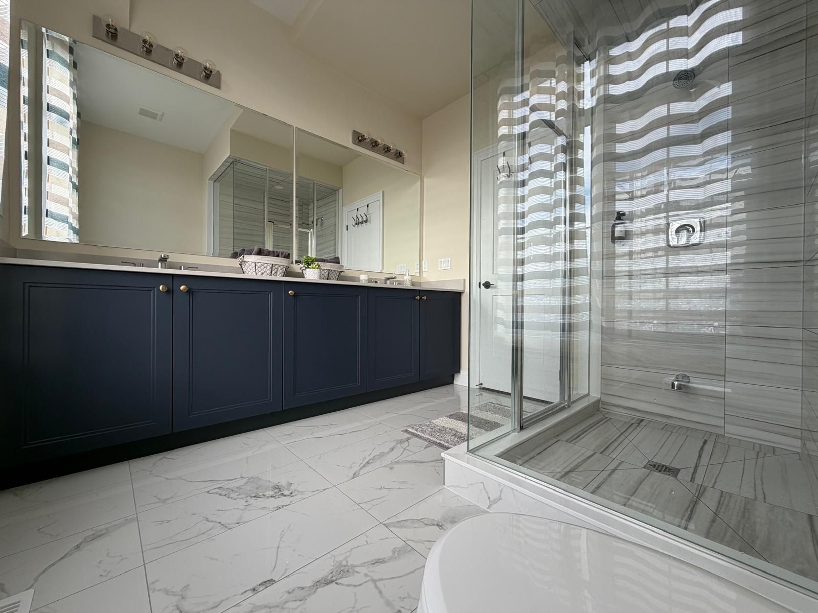 A modern bathroom with a dark blue vanity, a glass shower enclosure, and a marble floor.