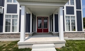 A two-story house with a red front door, white columns, and stone foundation.