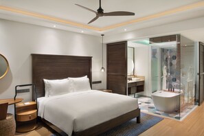 A modern hotel room with a large bed, a ceiling fan, a bathroom with a glass shower enclosure, and a wooden floor. - Intercontinental Dominica Cabrits Resort & Spa, an IHG Hotel (Portsmouth)