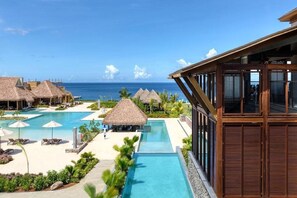 Un resort con piscina, edificaciones de techo de paja y vistas al océano.