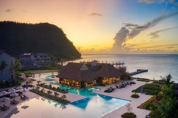 A resort with a swimming pool, thatched-roof structures, and a view of the sea at sunset. - Intercontinental Dominica Cabrits Resort & Spa, an IHG Hotel (Portsmouth)