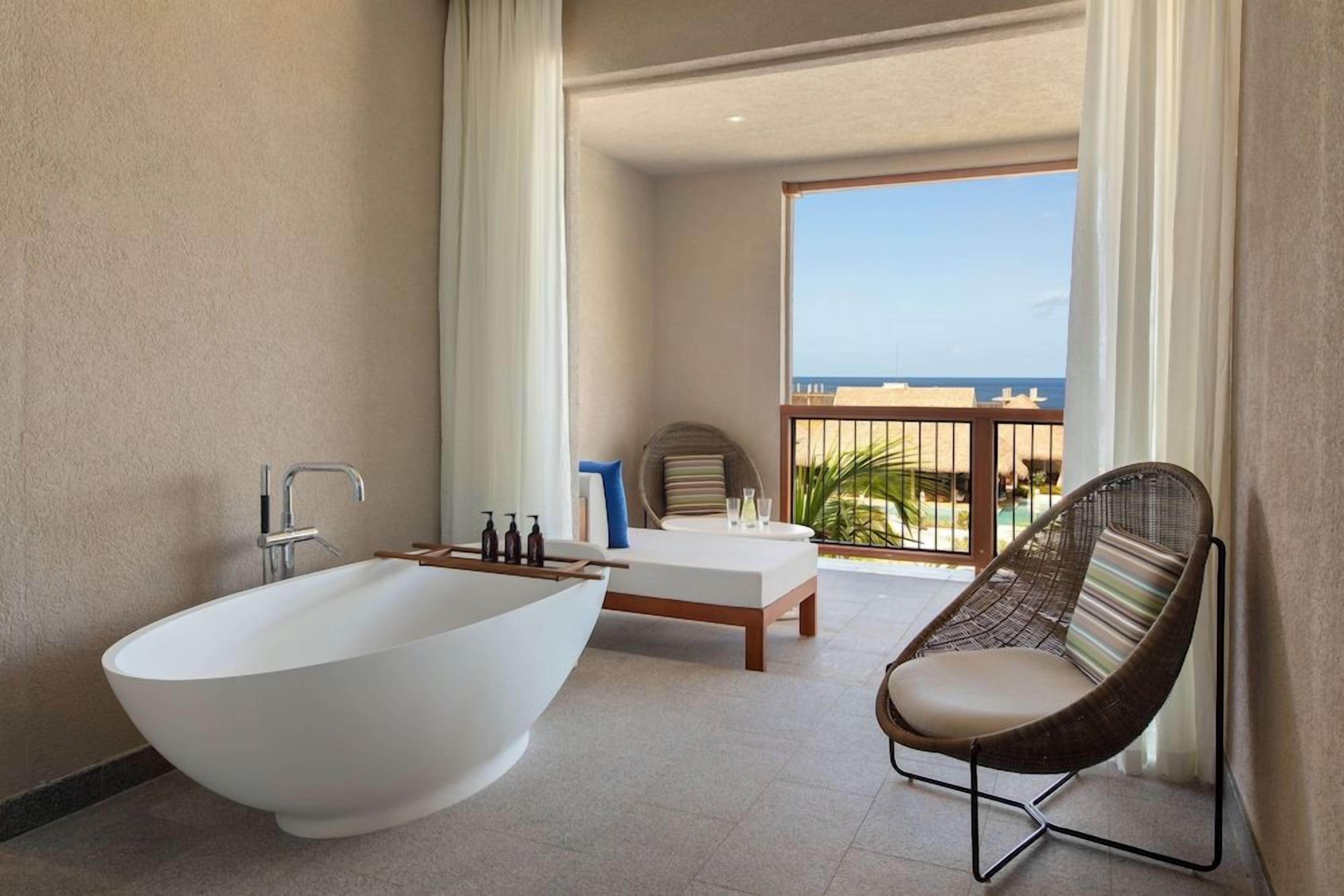 A modern bathroom with a freestanding bathtub, a wooden bench, and a wicker chair.
