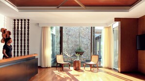 A modern reception area with a wooden reception desk, two wicker chairs, a potted plant, and a stone wall with a view of the outdoors.
