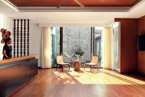 A modern reception area with a wooden reception desk, two wicker chairs, a potted plant, and a stone wall with a view of the outdoors. - Intercontinental Dominica Cabrits Resort & Spa, an IHG Hotel (Portsmouth)