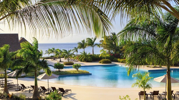 A resort pool with lounge chairs and palm trees.