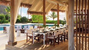 An outdoor dining area with a pool view, wooden deck, and thatched roof.