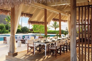 An outdoor dining area with a pool view, wooden deck, and thatched roof. - Intercontinental Dominica Cabrits Resort & Spa, an IHG Hotel (Portsmouth)