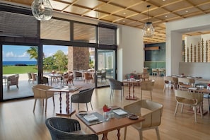 Un comedor amplio con varias mesas y sillas, ventanas grandes que ofrecen vistas al exterior, y un diseño de techo moderno.