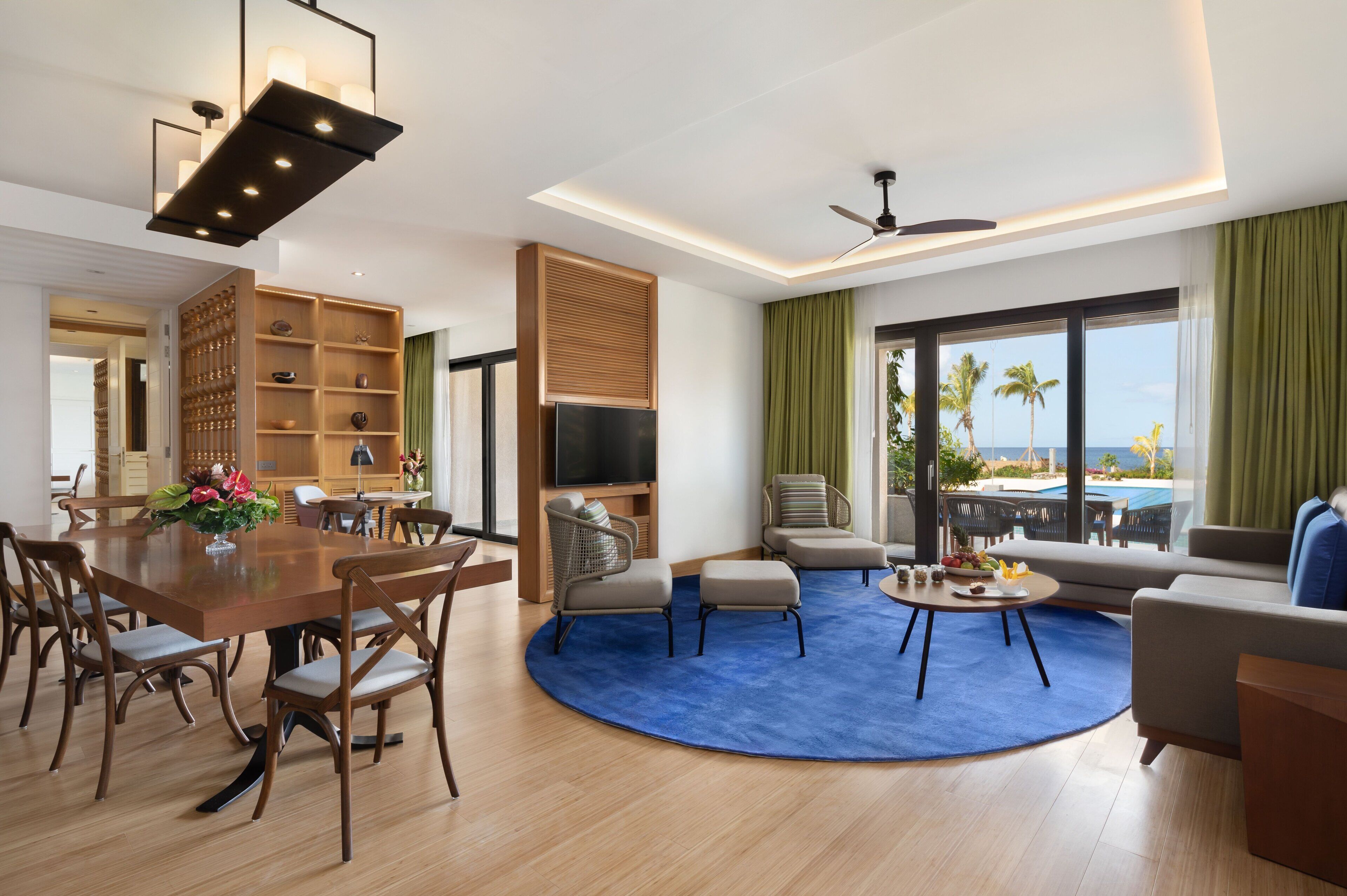 A modern hotel room with a dining area, seating, a TV, and a view of the ocean.