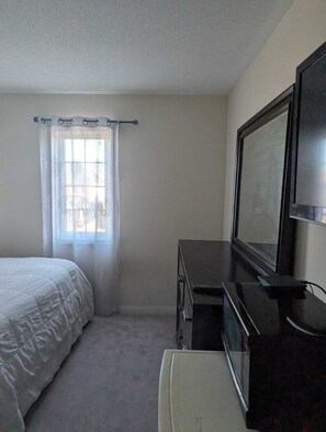 A bedroom with a bed, a television on a stand, and a window with curtains.