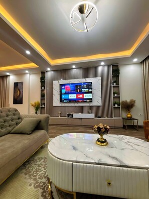 Ein modernes Wohnzimmer mit Sofa, rundem Couchtisch, einer Wandhalterung für den Fernseher und einer dekorativen Uhr an der Decke.
