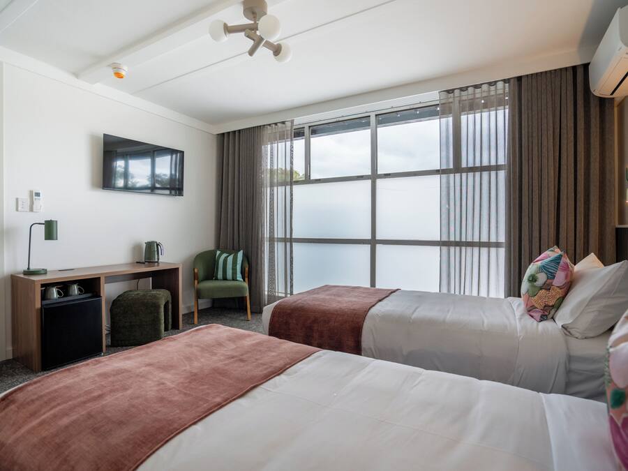 Habitación de hotel con dos camas, un escritorio, una silla, un televisor y un ventanal grande.