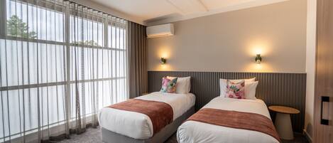 Une chambre d’hôtel avec deux lits, une fenêtre avec des rideaux, un appareil de climatisation et deux lampes fixées au mur.