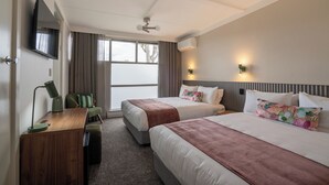 A hotel room with two beds, a desk with a lamp, a TV mounted on the wall, and a window with curtains. - Doonside Hotel Blacktown (Doonside)