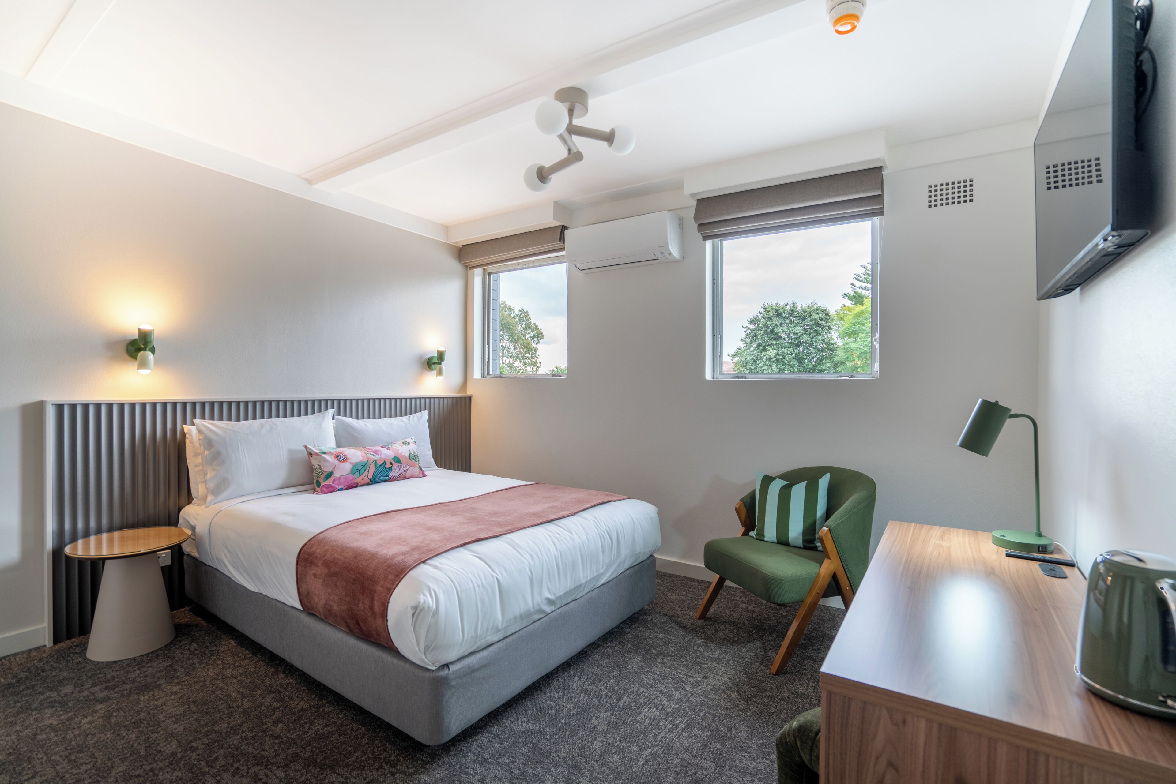 A hotel room with a bed, a desk, a chair, a TV, and a window.