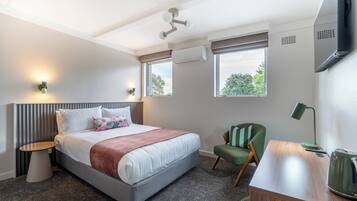 Ett hotellrum med en säng, ett skrivbord, en stol, en tv och ett fönster.