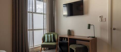 Una camera d'albergo con un letto, una scrivania con la televisione, una sedia, un piccolo tavolo e un armadio.