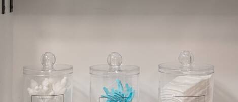 A shelf with a potted plant, three labeled containers with cotton swabs, floss picks, and cotton pads.