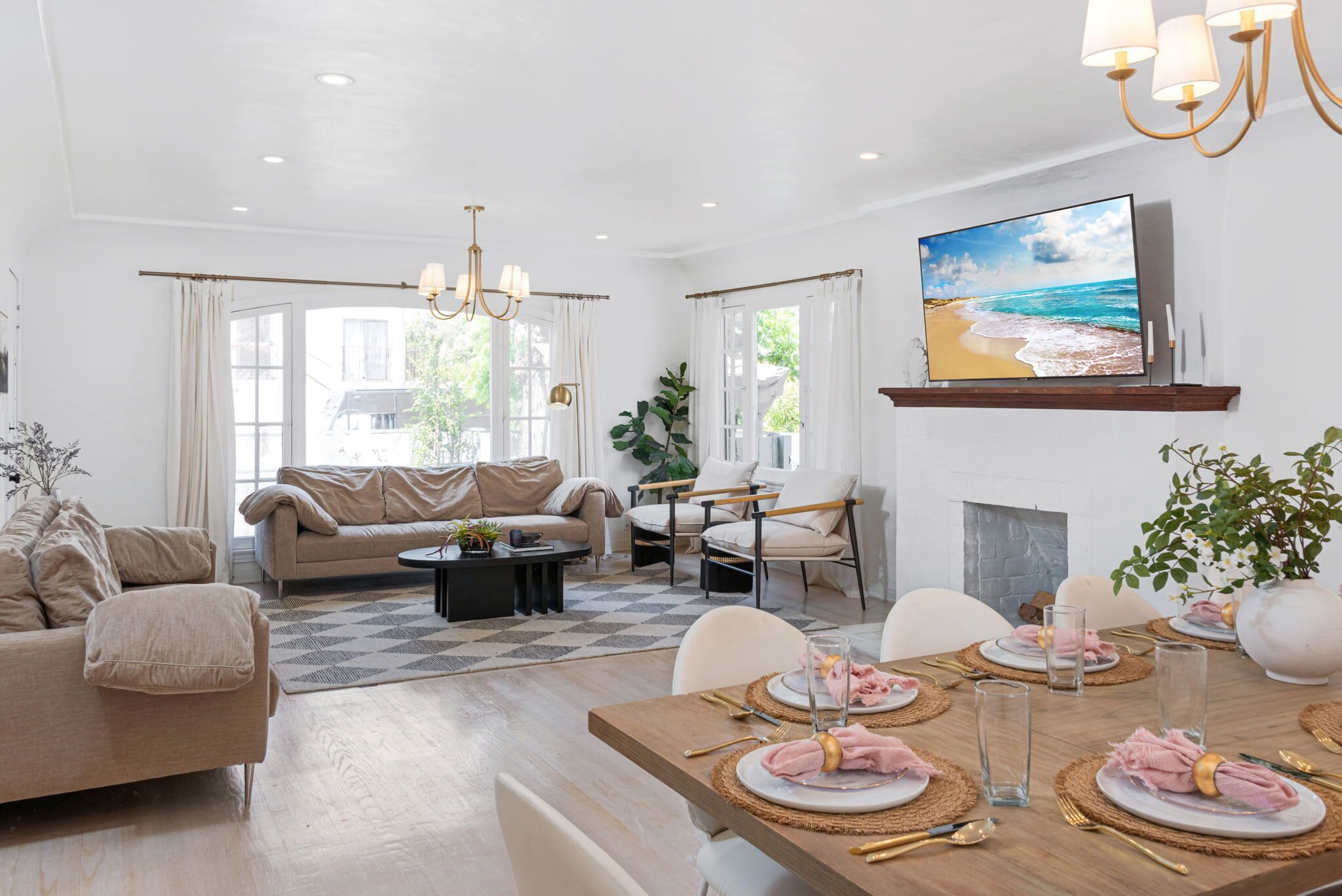 A modern living room with a sofa, coffee table, dining table set for four, and a TV mounted on the wall.. Remodeled Pico-Robertson Apt · 3BR + Parking