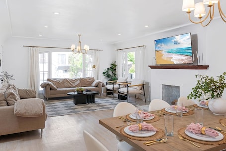 A modern living room with a sofa, coffee table, dining table set for four, and a TV mounted on the wall.. Remodeled Pico-Robertson Apt · 3BR + Parking