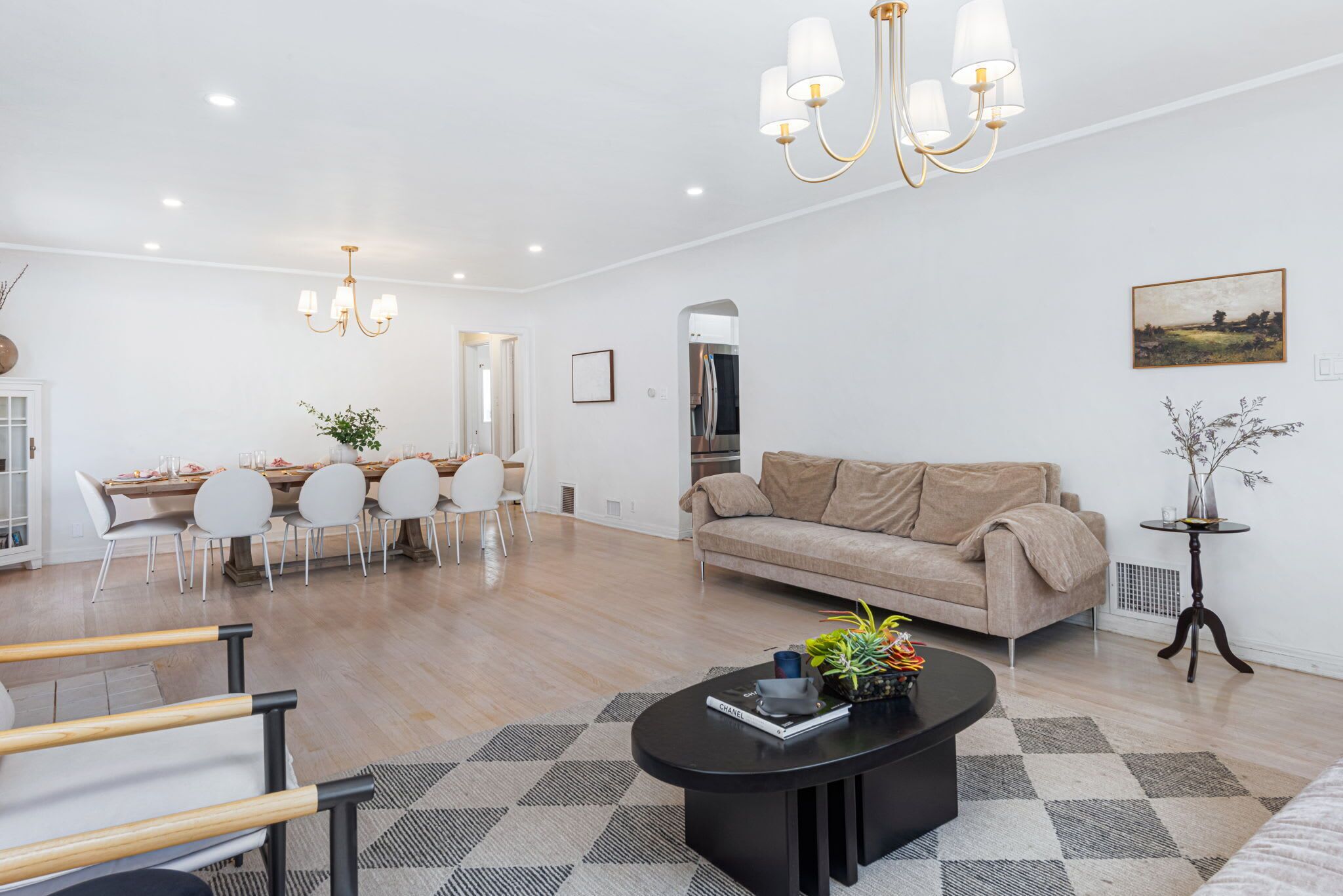 A modern living room with a sofa, coffee table, dining area, and a chandelier.