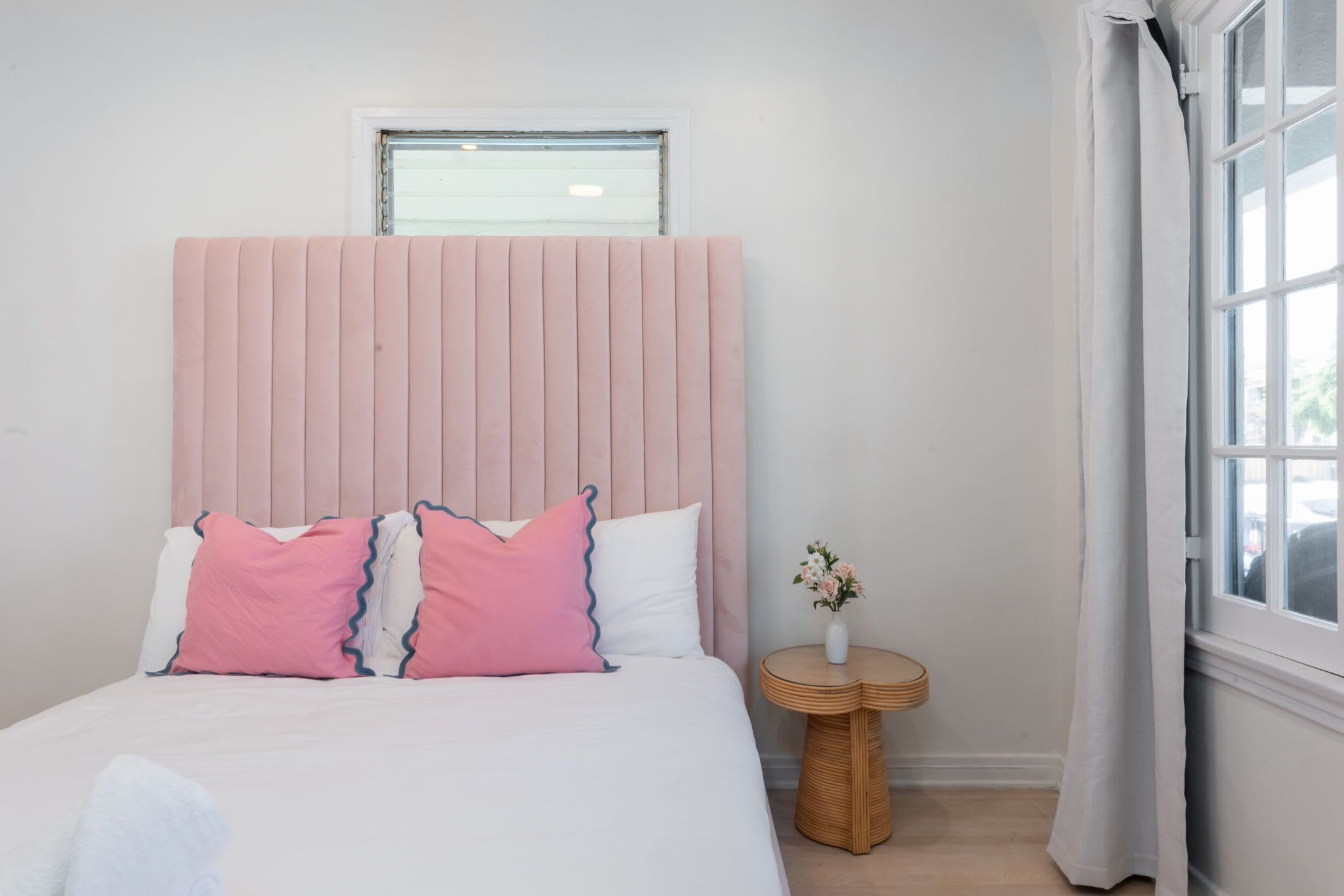 A bedroom with a bed, a bedside table with a vase, a window, and a curtain.