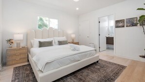 Un dormitorio con una cama grande, lámparas de noche, una mesita de noche, un espejo y una puerta que da a otra habitación.