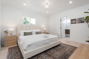 Un dormitorio con una cama grande, lámparas de noche, una mesita de noche, un espejo y una puerta que da a otra habitación.