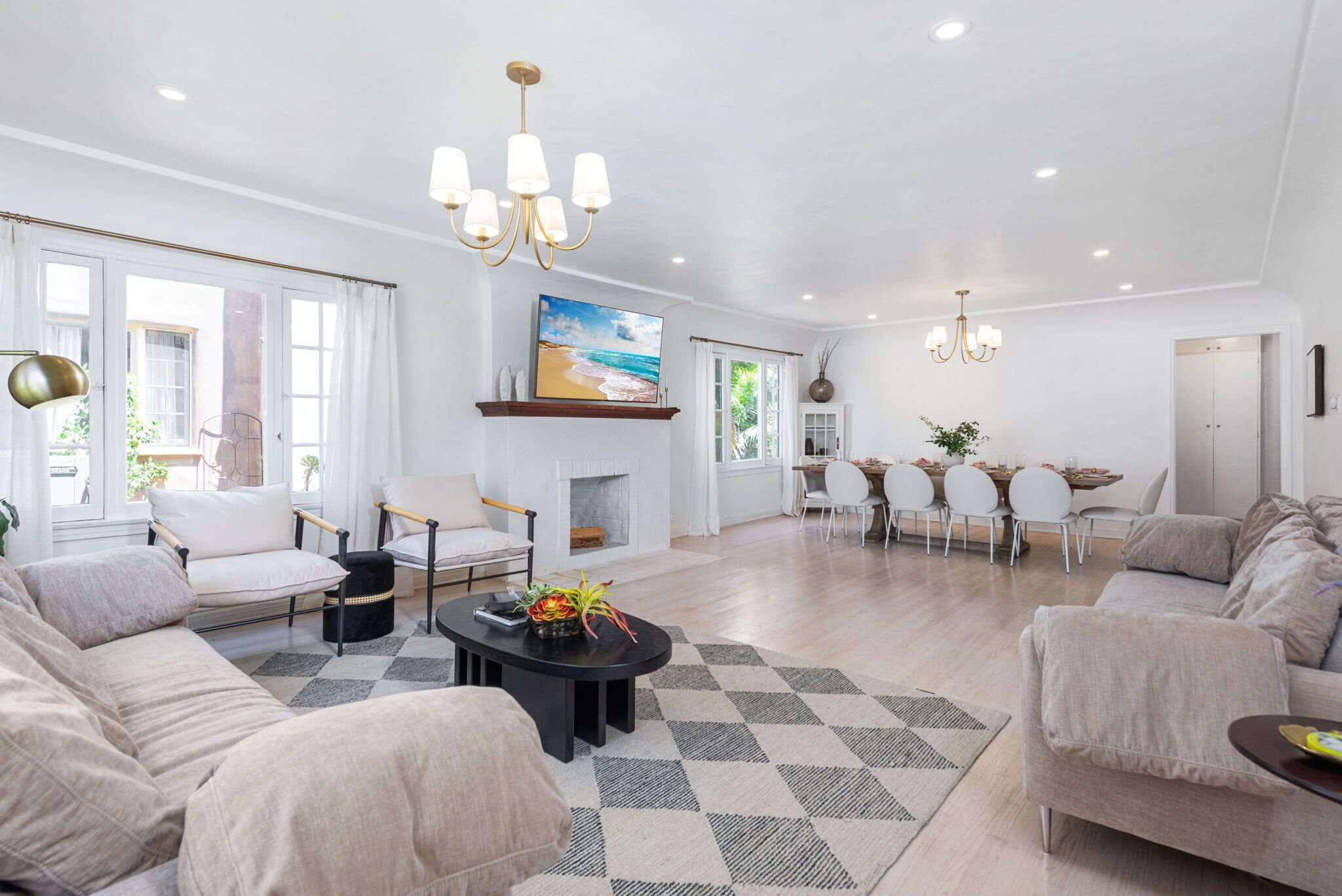 A spacious living room with a fireplace, a dining area with a table and chairs, and a large window with curtains.