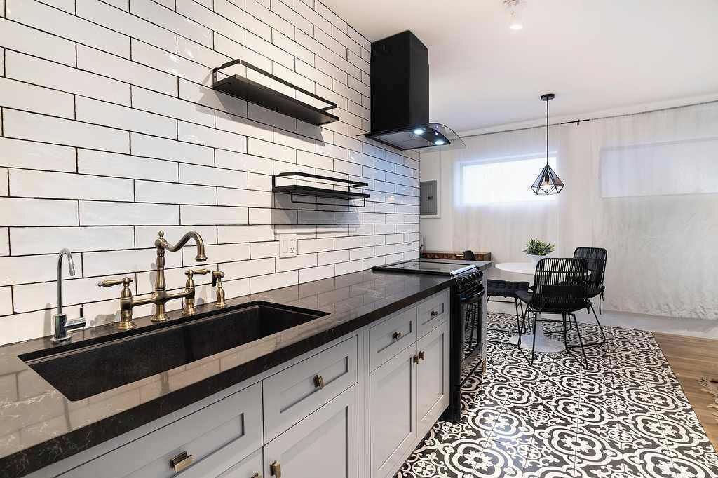 Una cocina moderna con azulejos blancos tipo metro, encimera negra y campana extractora negra.