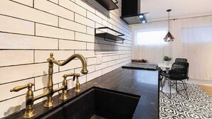 Een moderne keuken met zwarte aanrechtbladen, een witte betegelde spatwand en een zwarte eethoek met een kamerkleed met patroon.