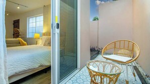 Een slaapkamer met een bed, een schuifpui, een rieten stoel en een tafeltje.