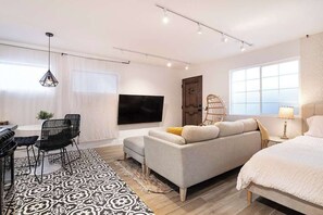 Une chambre d’hôtel moderne équipée d’un canapé, d’un lit, d’une télévision, d’un coin repas avec des chaises et d’un tapis à motifs.